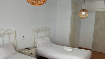 Two single beds with white linens and towels, a bedside table with a remote control, and a wall-mounted phone.