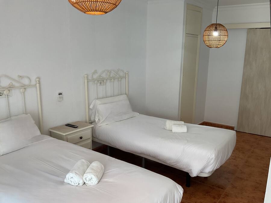 Two single beds with white linens and towels, a bedside table with a remote control, and a wall-mounted phone.