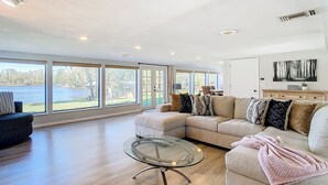 Amplia sala de estar con ventanas grandes, un sofá modular, una mesa de centro de vidrio y vista a un lago.