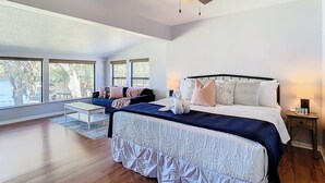 Un dormitorio amplio con una cama grande, un ventilador de techo y vistas a un lago a través de amplios ventanales.
