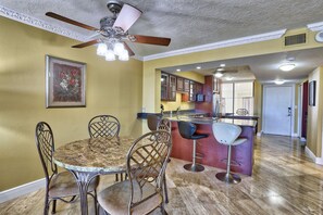 A dining area with a round table and four chairs, a ceiling fan, and a kitchen in the background. - St. Pete Beach Yacht and Tennis Club 404 (St. Pete Beach)