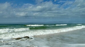 A beach with waves crashing onto the shore under a cloudy sky.
