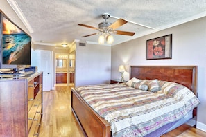 A bedroom with a wooden bed, a ceiling fan, a TV, and a painting on the wall. - St. Pete Beach Yacht and Tennis Club 404 (St. Pete Beach)
