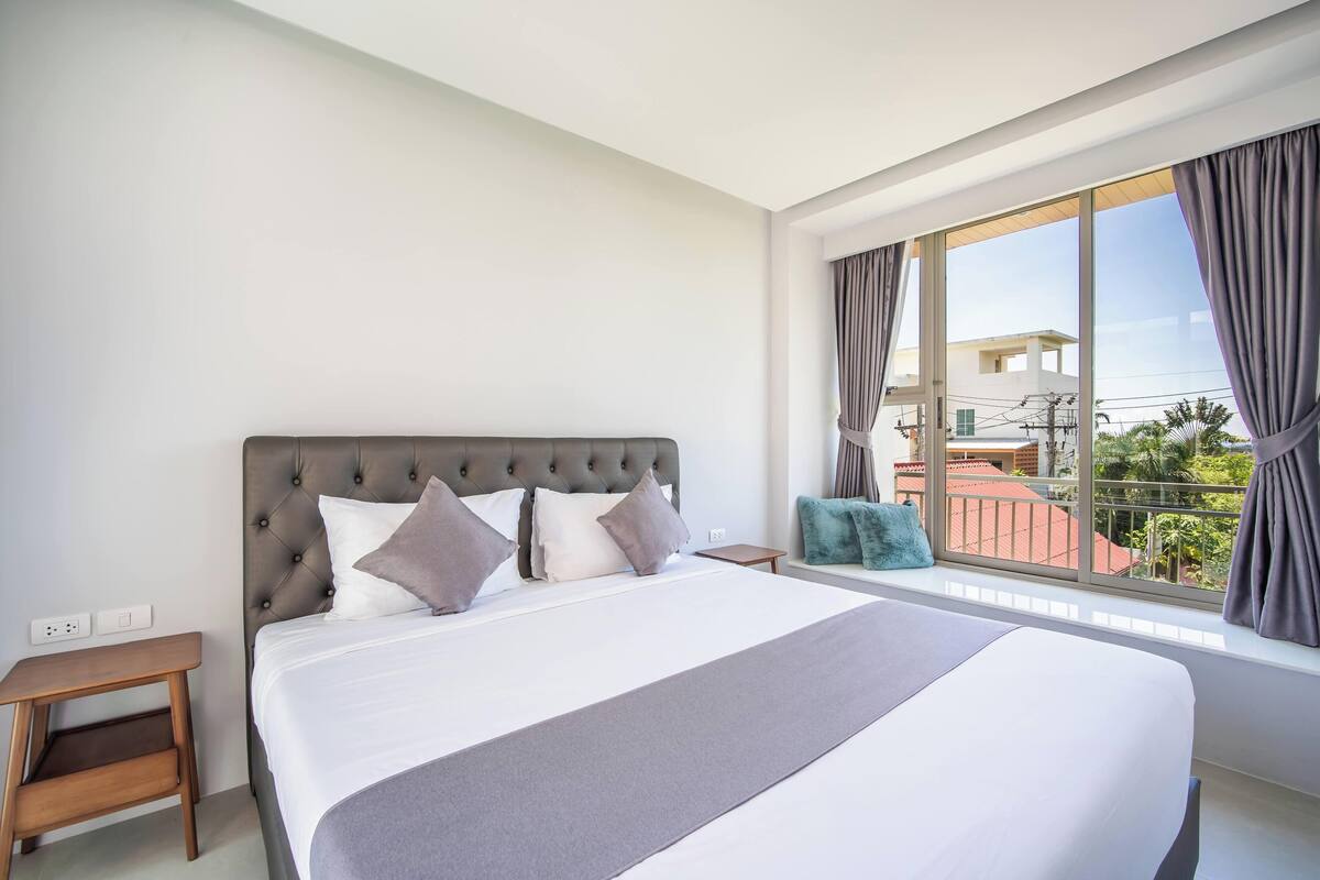 A modern hotel room with a large bed, a small side table, and a window with curtains.