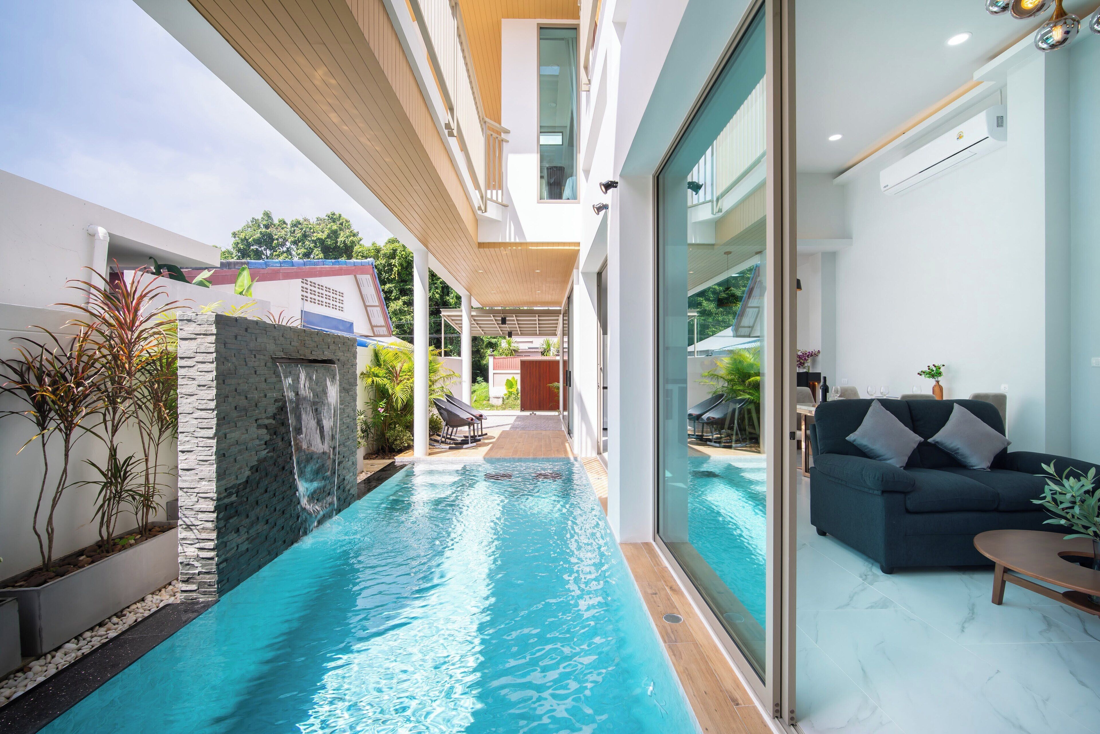 Piscina interior moderna com parede de pedra, teto de madeira e um sofá com almofadas.