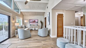 Un'ampia zona giorno con soffitto alto, pavimento in legno e un grande schermo televisivo.