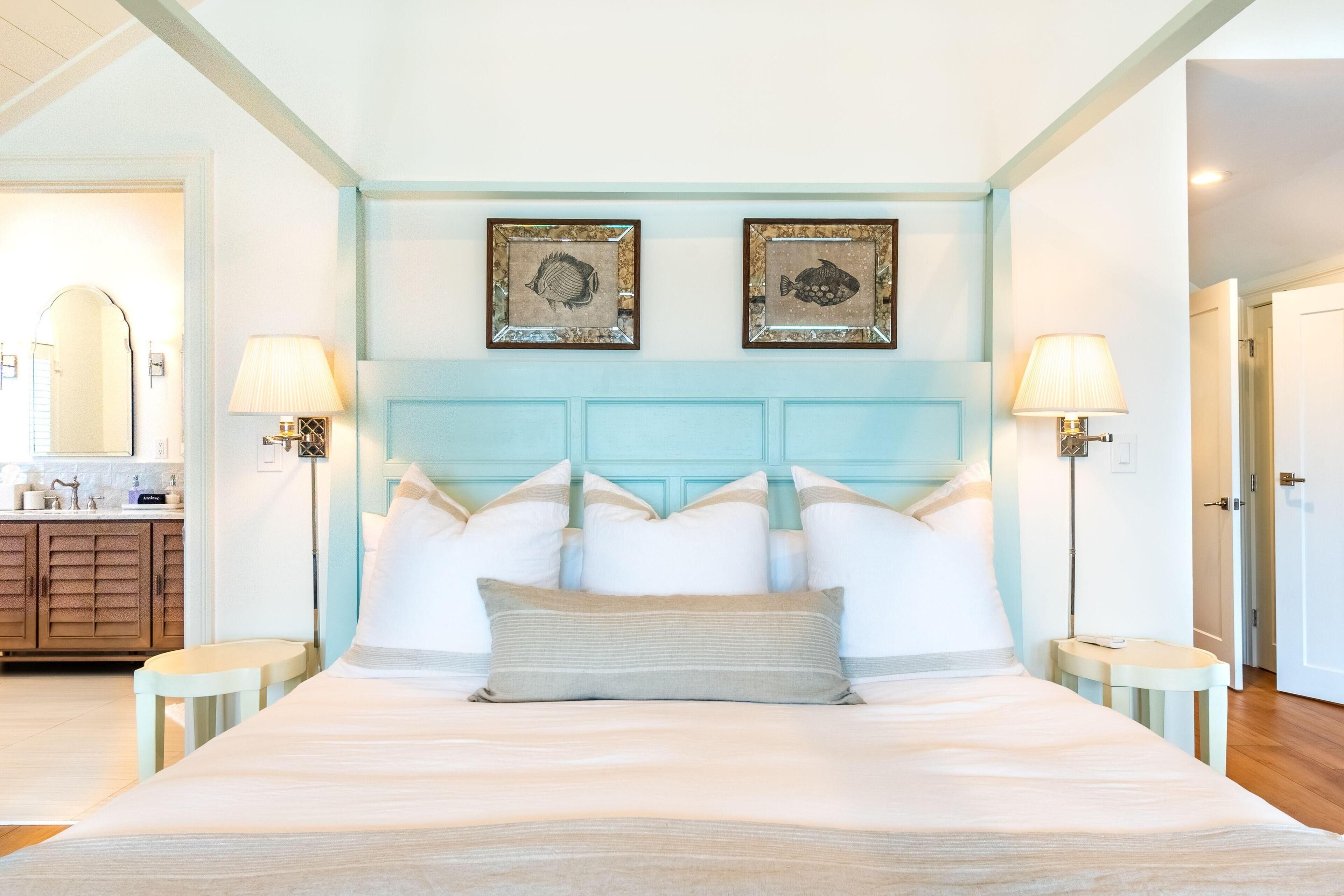 A large bed with a light blue headboard, two framed fish pictures, and bedside lamps.