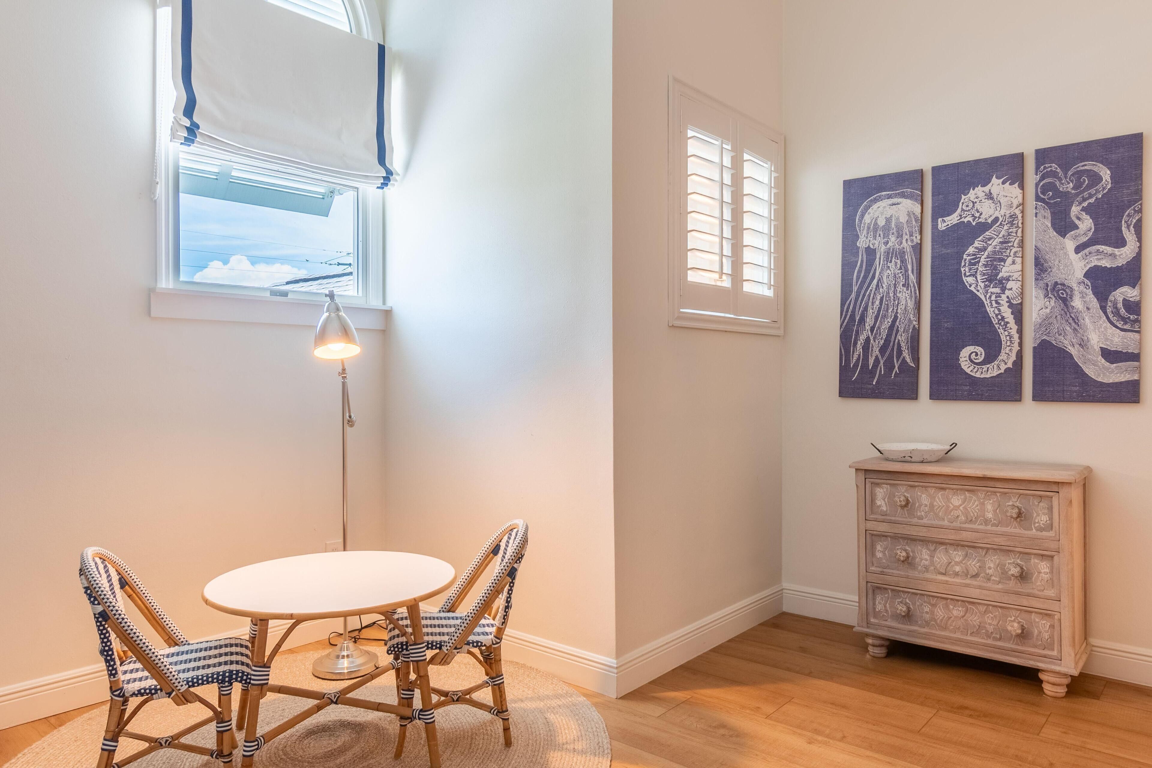 A room with a round table, two wicker chairs, a floor lamp, a dresser, and three wall-mounted seahorse paintings.