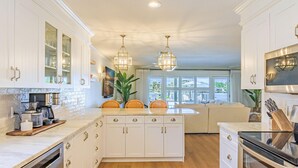 Una cocina moderna con armarios blancos, una isla central y un comedor con sofá.