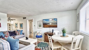 A living room with a sofa, coffee table, and a dining area with chairs and a table. There is a painting on the wall and a plant on the table. - Friendly Native 204 (St. Pete Beach)