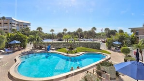 A swimming pool with a curved edge, surrounded by lounge chairs and umbrellas. - Friendly Native 204 (St. Pete Beach)