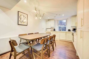 A dining area with a wooden table and chairs, a kitchen with white cabinets, and a framed artwork on the wall.