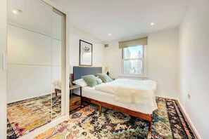 A bedroom with a bed, a window, a mirror, and a patterned rug.