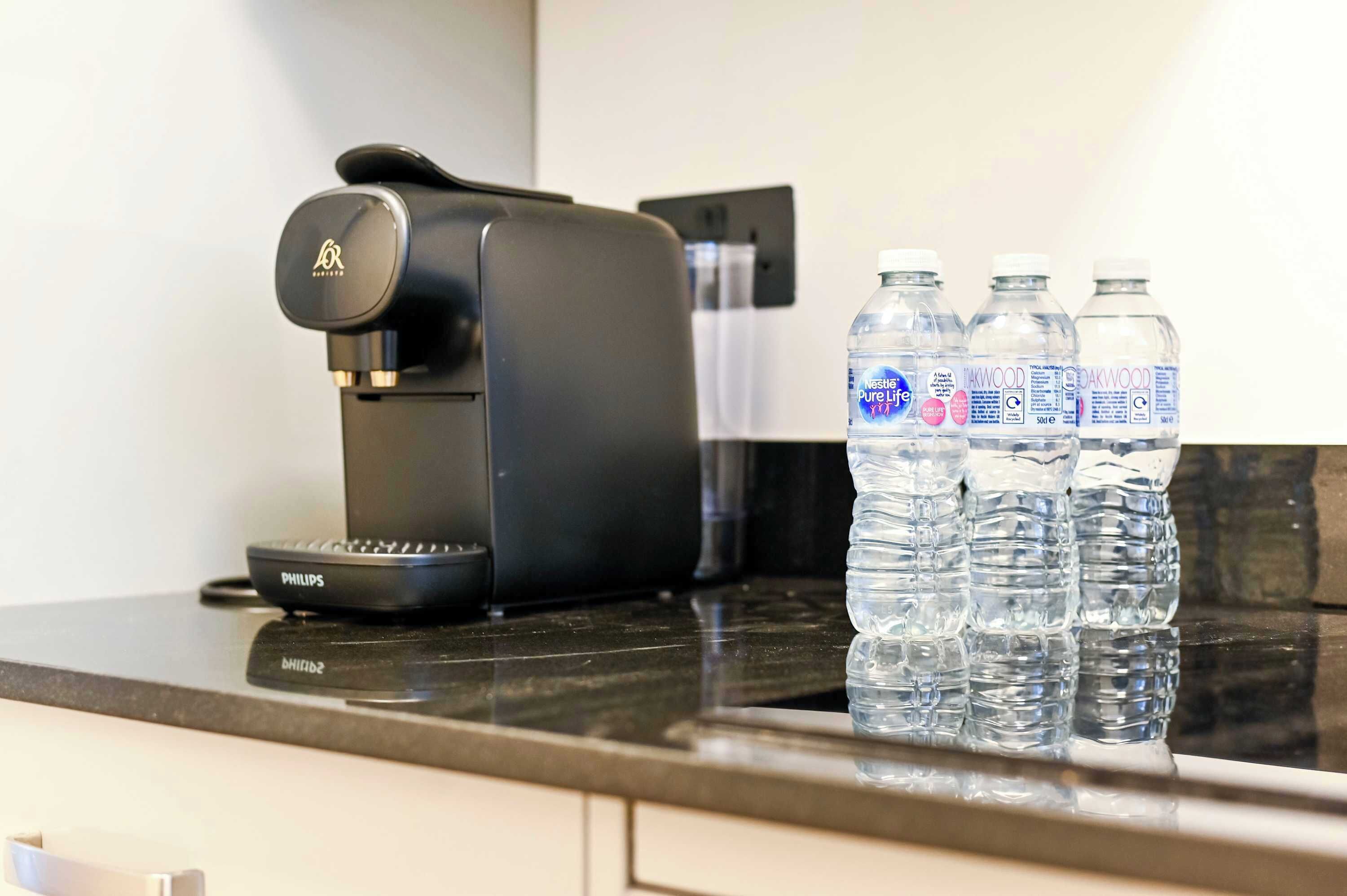 Eine Kaffeemaschine und drei Wasserflaschen auf einer Küchenarbeitsplatte.