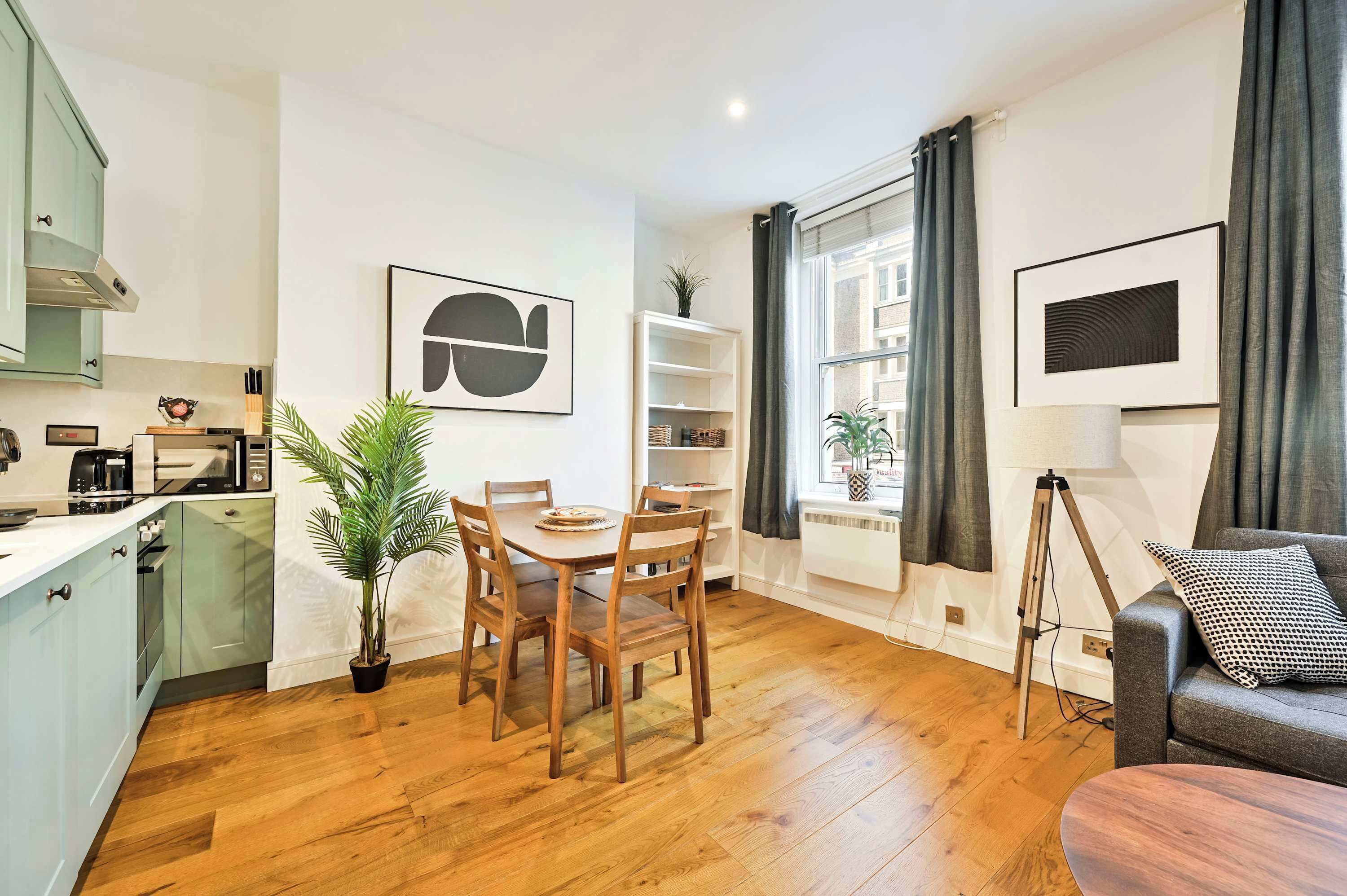 A modern kitchen with a dining area, wooden flooring, and a view of the city through large windows.