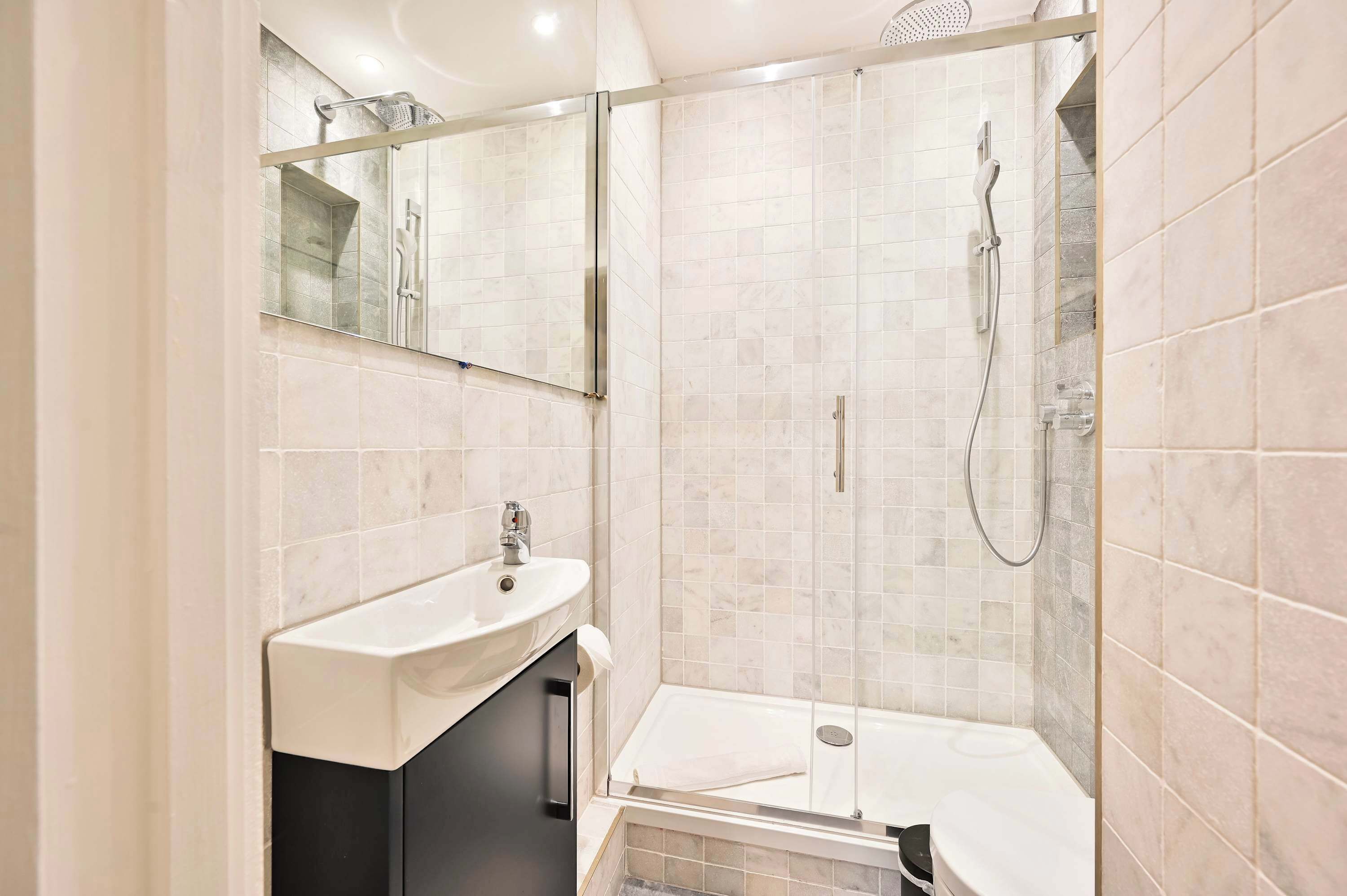Une salle de bain moderne avec une douche à parois de verre, un lavabo blanc et un miroir au-dessus.