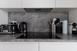 Eine moderne Küche mit einer schwarzen Induktionskochplatte, einem Breville-Toaster, einer Kaffeemaschine und einem Reiskocher.