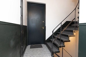 Eine schwarze Tür mit Knauf und Fußmatte am unteren Ende einer Treppe mit Metallgeländer.