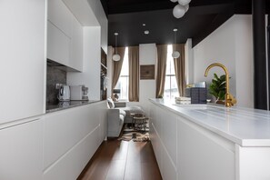 A modern kitchen with white cabinetry, a central island, a gold faucet, and a dining area with a sofa and table. - Superb 1 Bedroom Apartment Holborn London (London)
