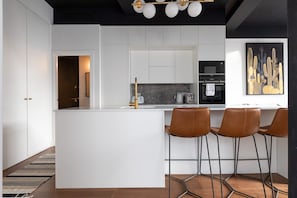 A modern kitchen with white cabinetry, a central island with bar stools, a coffee machine, and a microwave.