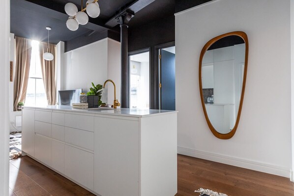 A modern kitchen with a white countertop, gold faucet, and a large mirror with a wooden frame.