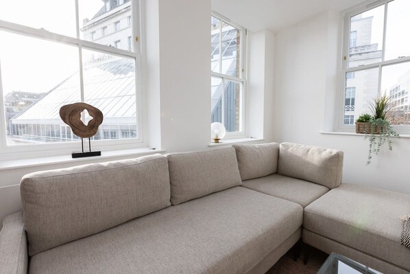 Una sala de estar moderna con un sofá seccional color beige, ventanas amplias y un adorno de pared decorativo.