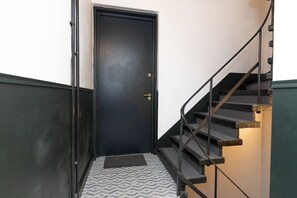 Eine schwarze Tür mit Knauf und Fußmatte am unteren Ende einer Treppe mit Metallgeländer.