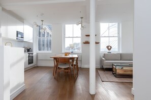 Una cocina moderna con armarios blancos, un comedor con mesa y sillas de madera, y una sala de estar con sofá y una mesa de centro.