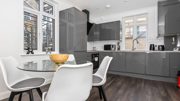 A modern kitchen with grey cabinets, a glass dining table, and two white chairs. - Outstanding 2 Bed Apartment in  Camden Sleeps 6 (London)