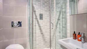 Un baño moderno con ducha envuelta en vidrio, inodoro blanco y lavamanos con dos dispensadores de jabón.