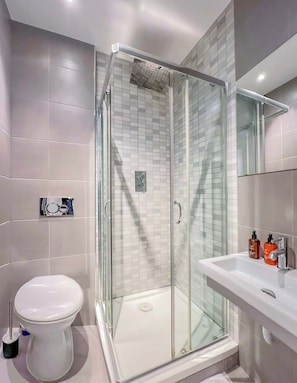 Un baño moderno con ducha envuelta en vidrio, inodoro blanco y lavamanos con dos dispensadores de jabón.