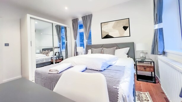 Un dormitorio moderno con una cama grande, mesitas de noche, un espejo y vistas a la ciudad.