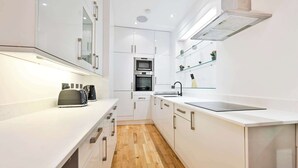 Eine moderne Küche mit weißen Schränken, Holzboden, einem eingebauten Backofen und einer eleganten Arbeitsplatte.