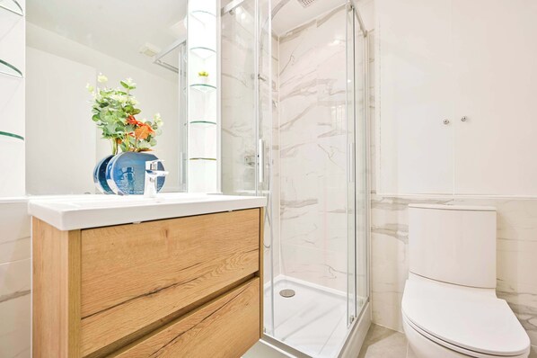 A modern bathroom with a glass shower enclosure, a white toilet, and a wooden vanity with a vase of flowers.