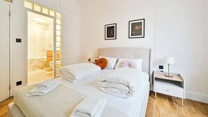 Ein modernes Hotelzimmer mit zwei Betten, einem Badezimmer mit Duschkabine und einem Nachttisch mit Lampe.