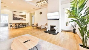A modern living room with a wooden floor, a round coffee table, a fireplace, a TV, and a large plant. - Amazing 3 Bed Apartment Great Portland Street (Greater London)