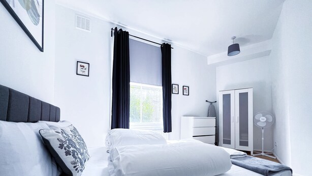 Een netjes ingerichte slaapkamer met een bed, een dressoir, een kledingkast en een ventilator.