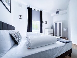 A neatly arranged bedroom with a bed, a dresser, a wardrobe, and a standing fan. - Cosy Camden Apartment (London)