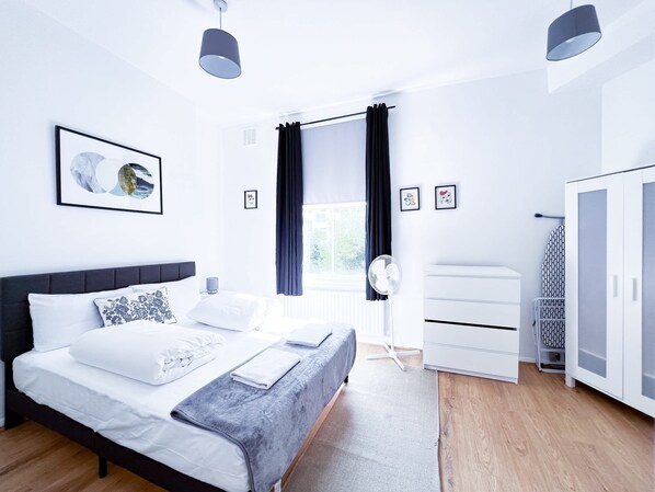 A modern bedroom with a bed, bedside tables, a wardrobe, and a window with curtains. - Cosy Camden Apartment (London)