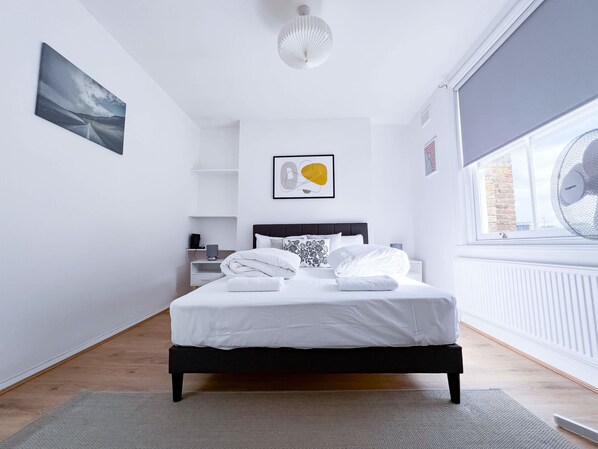 Une chambre à coucher moderne, avec un lit, des tables de chevet, une fenêtre donnant sur un beau paysage et des œuvres d’art accrochées aux murs.