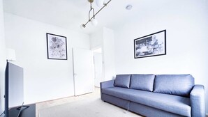 Un salon moderne avec un canapé gris, un téléviseur à écran plat et deux œuvres d’art encadrées accrochées aux murs.