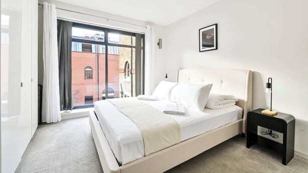 Een moderne slaapkamer met een groot bed, een nachtkastje met een lamp en een raam met gordijnen.