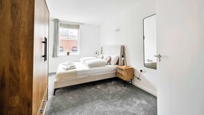 Ein Schlafzimmer mit Bett, Nachttisch, Kleiderschrank, Fenster und Spiegel.