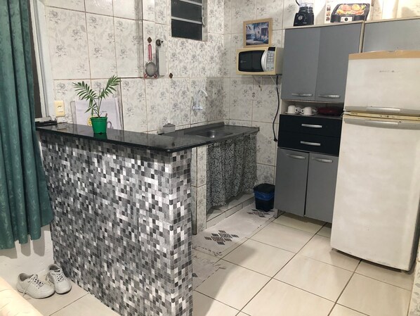 A kitchen with a tiled backsplash, a small island, a microwave, a refrigerator, and a sink. - Cozy Apartment in Salvador (Campinas de Brotas Salvador)