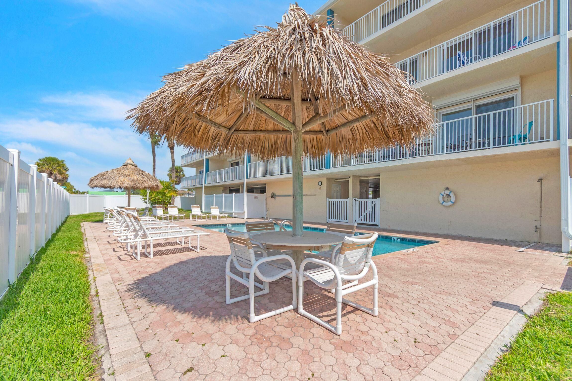 A pool area with lounge chairs and a thatched umbrella, surrounded by a building with balconies.