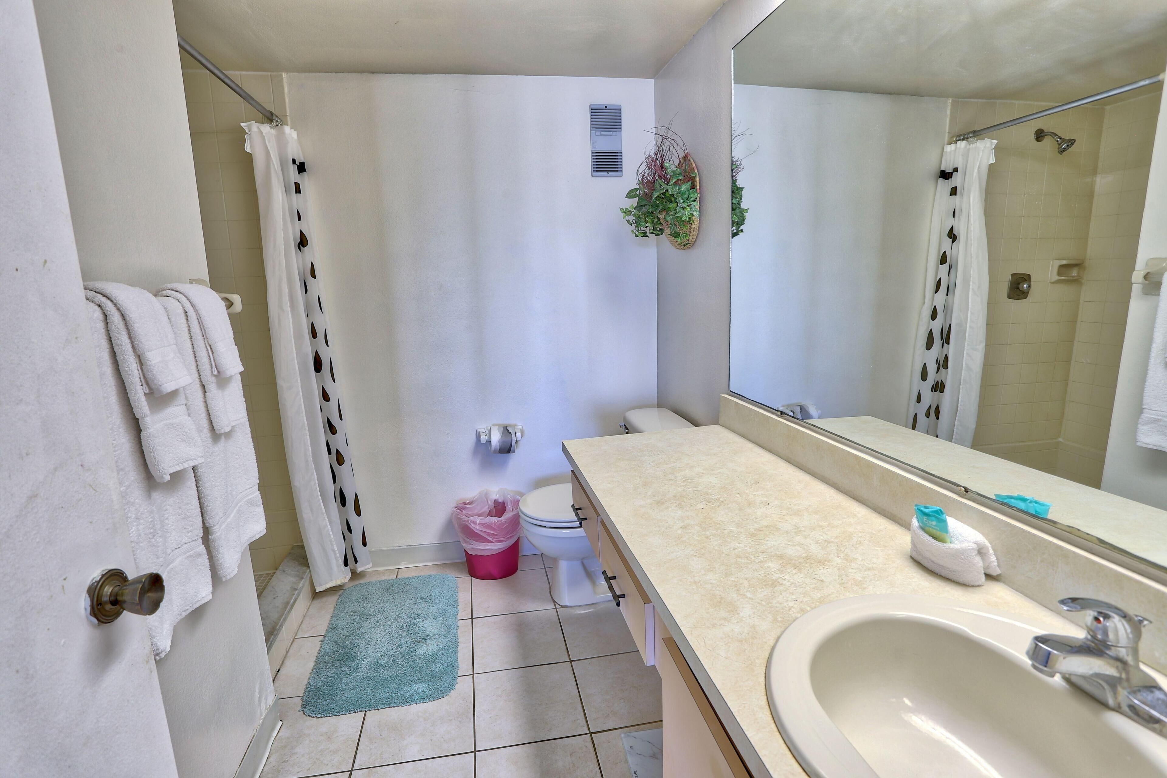 A bathroom with a beige sink, a mirror, a toilet, and a shower area.