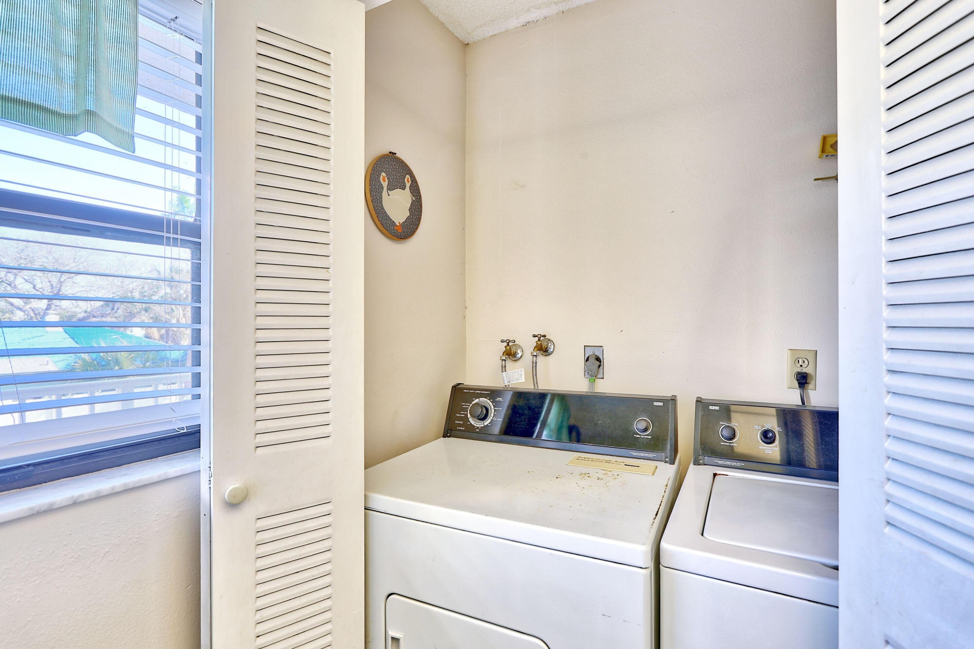A laundry room with two washing machines, a towel rack, and a window with blinds.