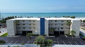 Ein mehrstöckiges Hotel mit blauem zentralem Akzent, Parkplatz und Blick auf den Strand.
