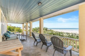 A covered patio with a view of the beach, featuring outdoor seating and a table. - Beachside Vista (New Smyrna Beach)