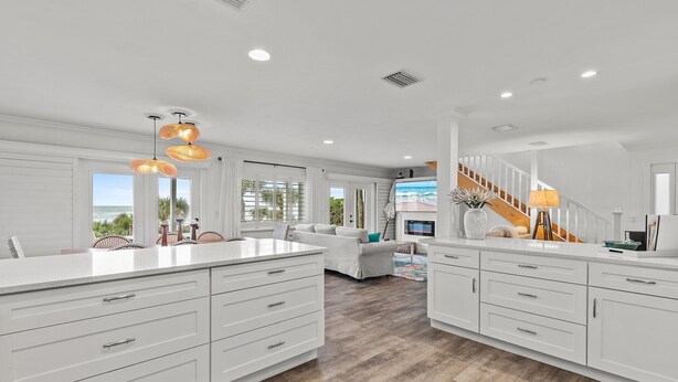 A spacious kitchen with white cabinetry, a large island, and a wooden staircase leading to a balcony. - Blue Yonder Beach House (New Smyrna Beach)